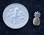 tiny metal pineapple next to a dime